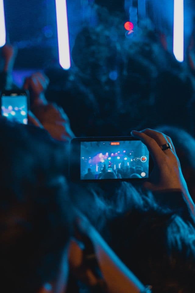 Close-up of a smartphone recording a blue-lit stage from inside a club crowd