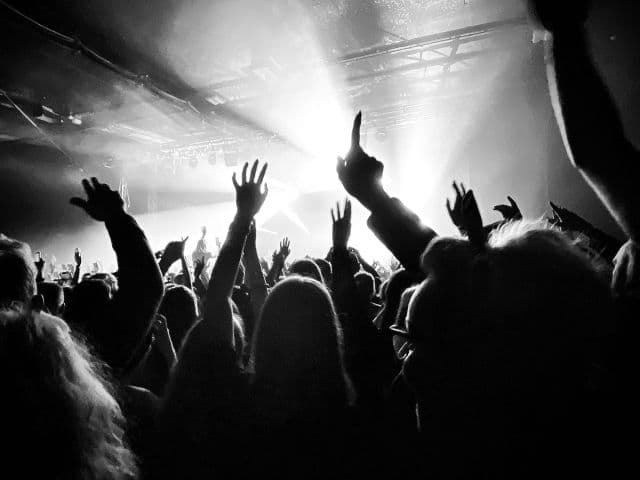 Black-and-white photo of a packed crowd with hands raised toward bright stage lights