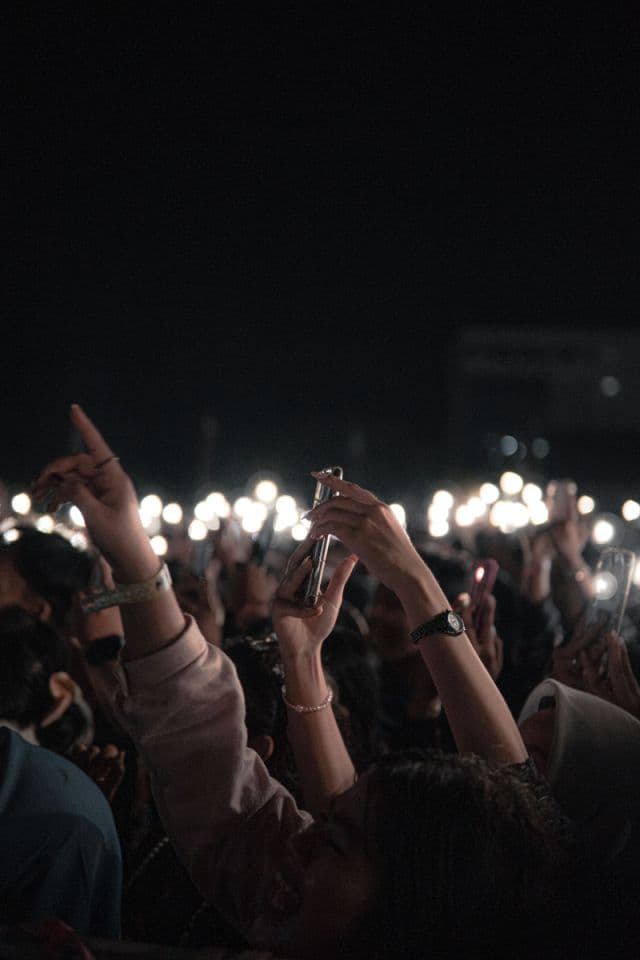 Crowd at a nighttime show with phones held up toward the stage