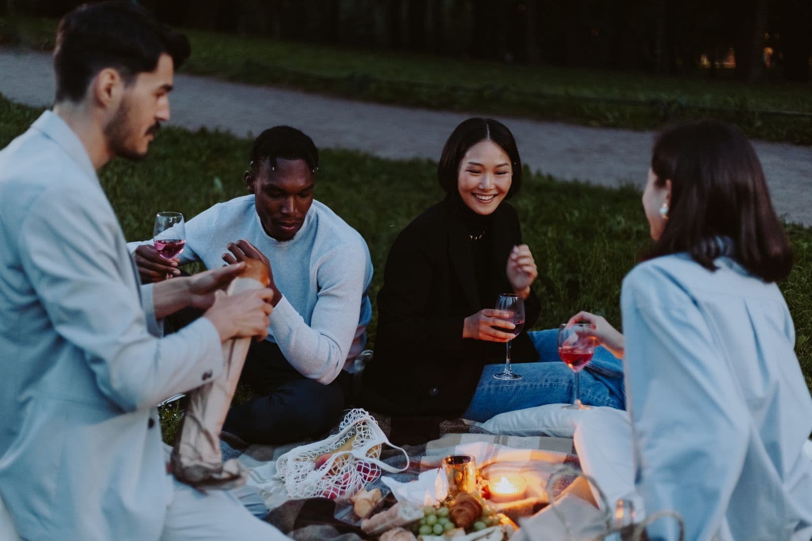 Group of friends talking over wine at an evening picnic in a park