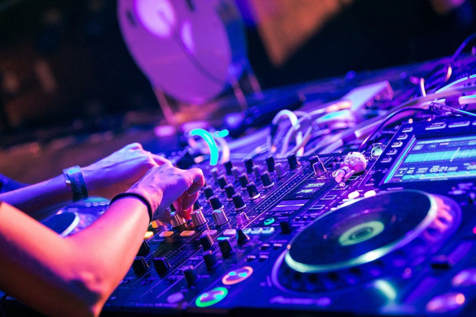 A DJ's hands on a controller lit by purple light