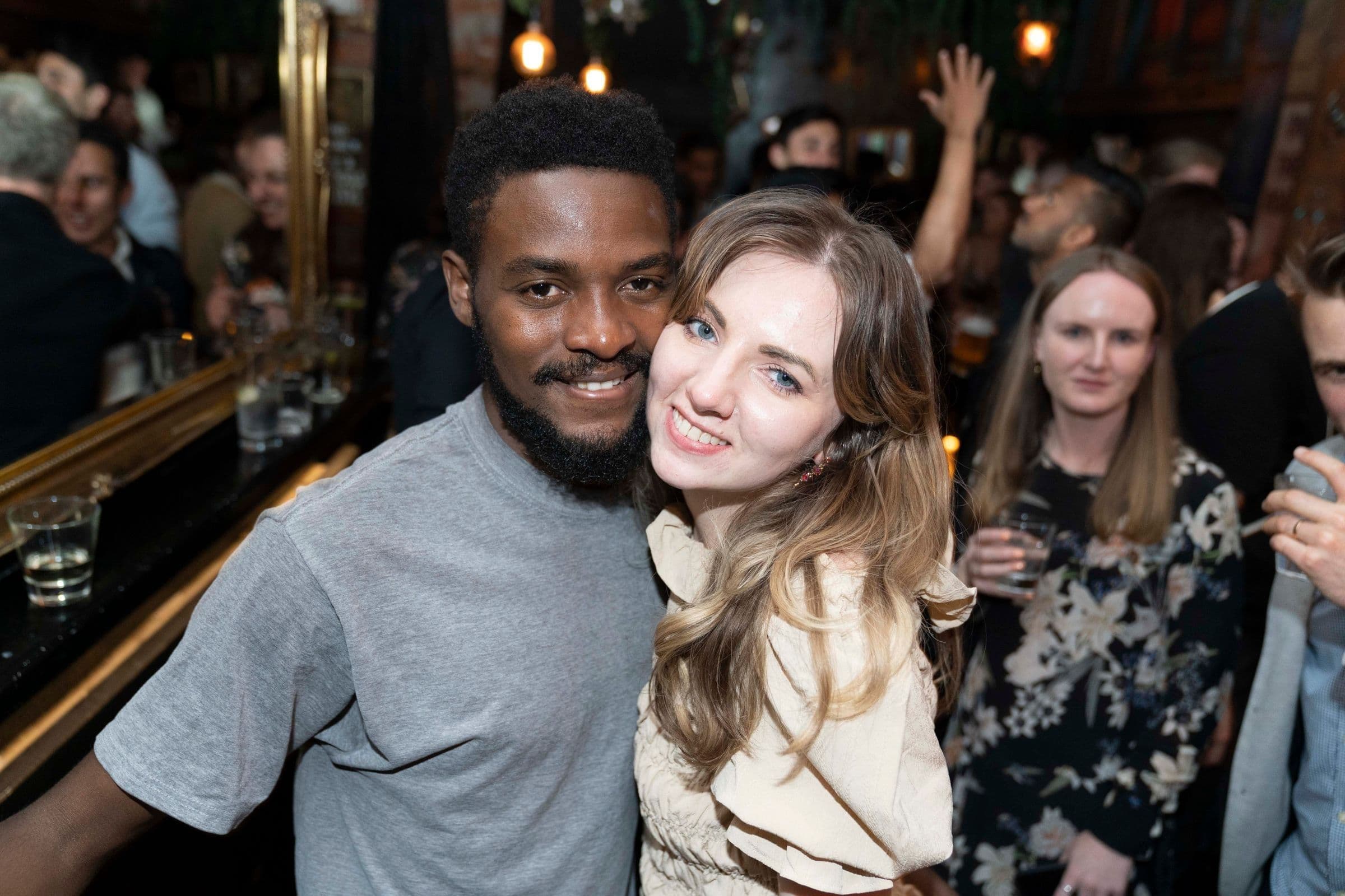 A diverse group of friends smiling close together in a packed, warmly lit bar
