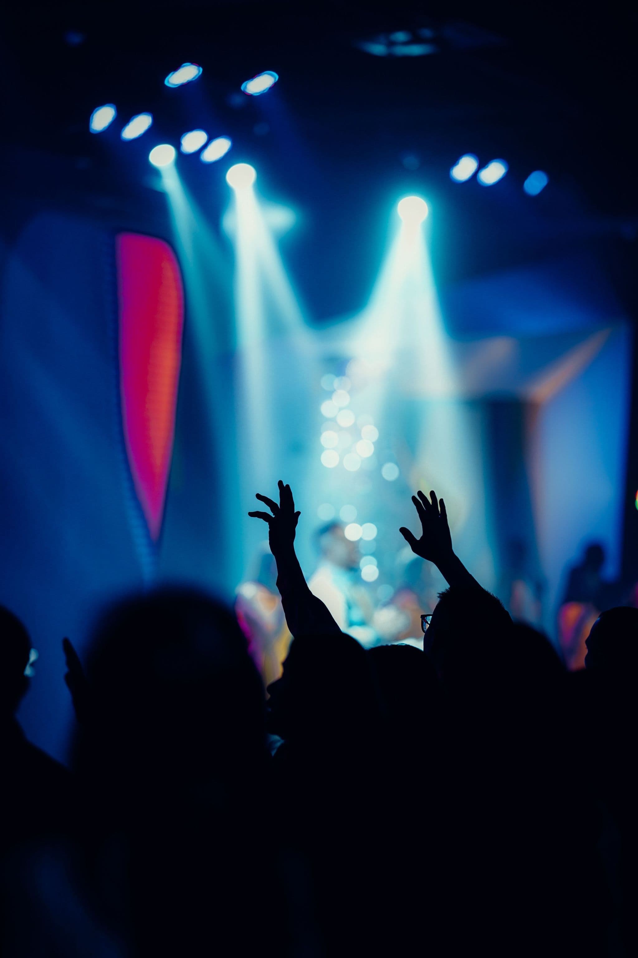 Silhouetted crowd with two hands raised toward a blue-lit stage at a night show