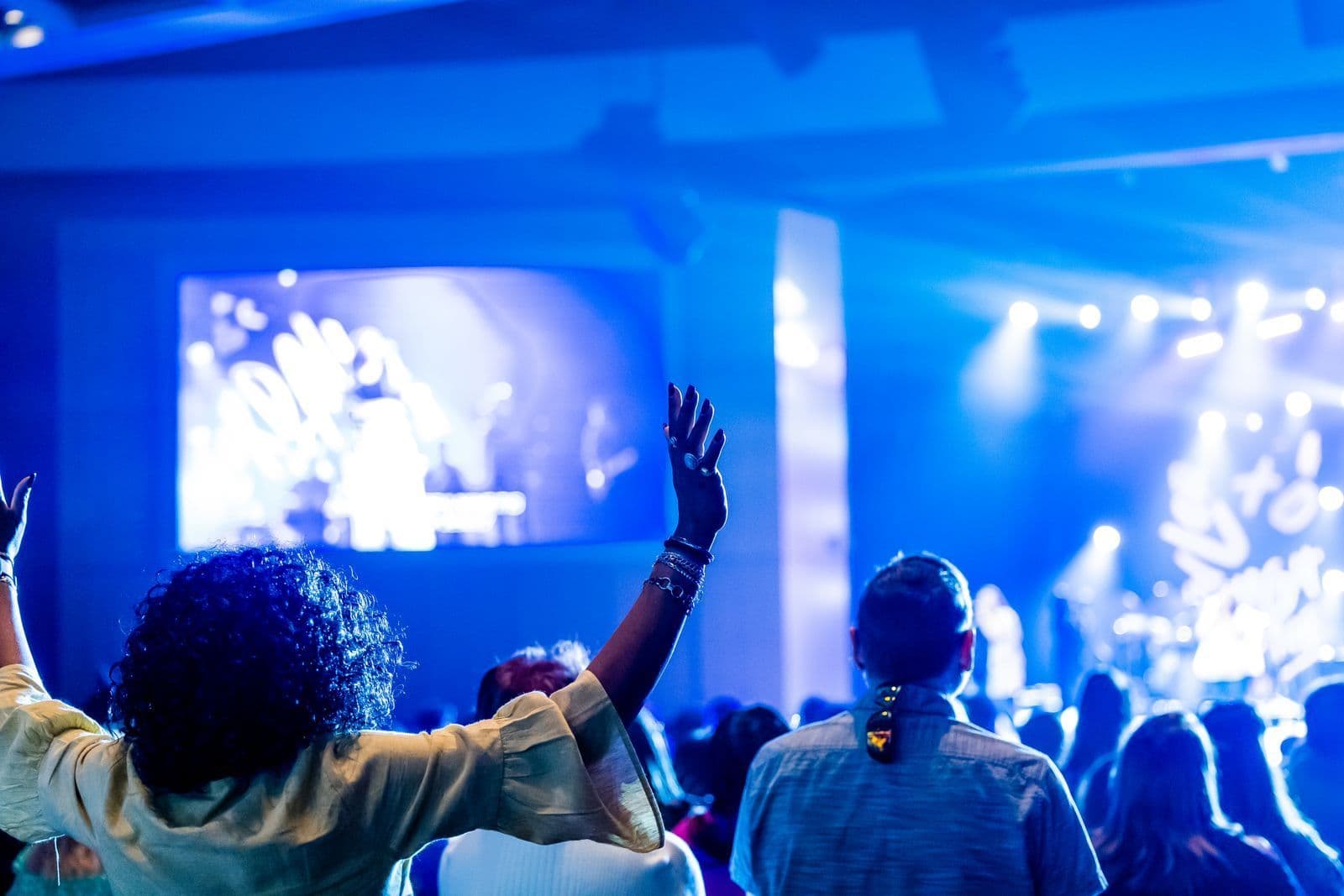 A crowd with hands up in front of a blue-lit stage