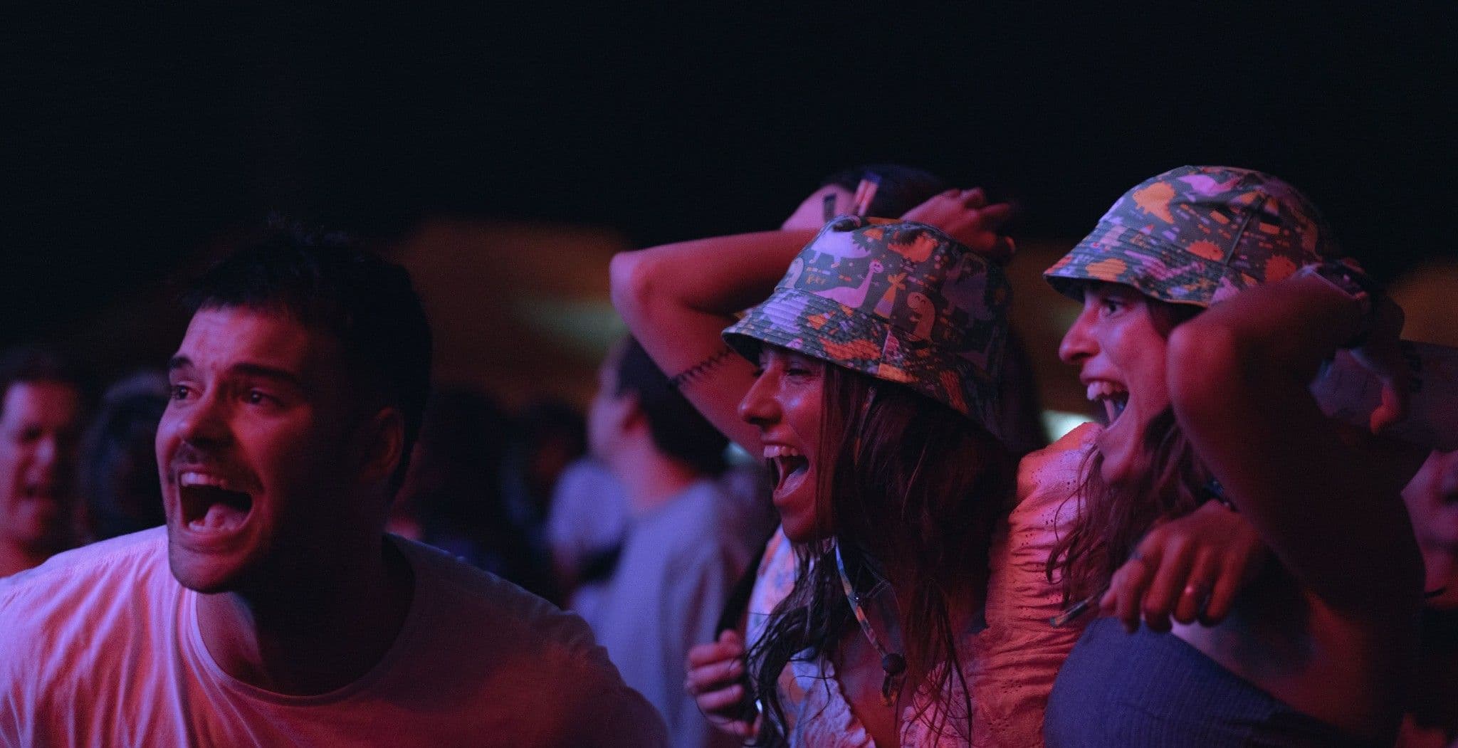 Three friends cheering in the crowd at a night show, two in bucket hats