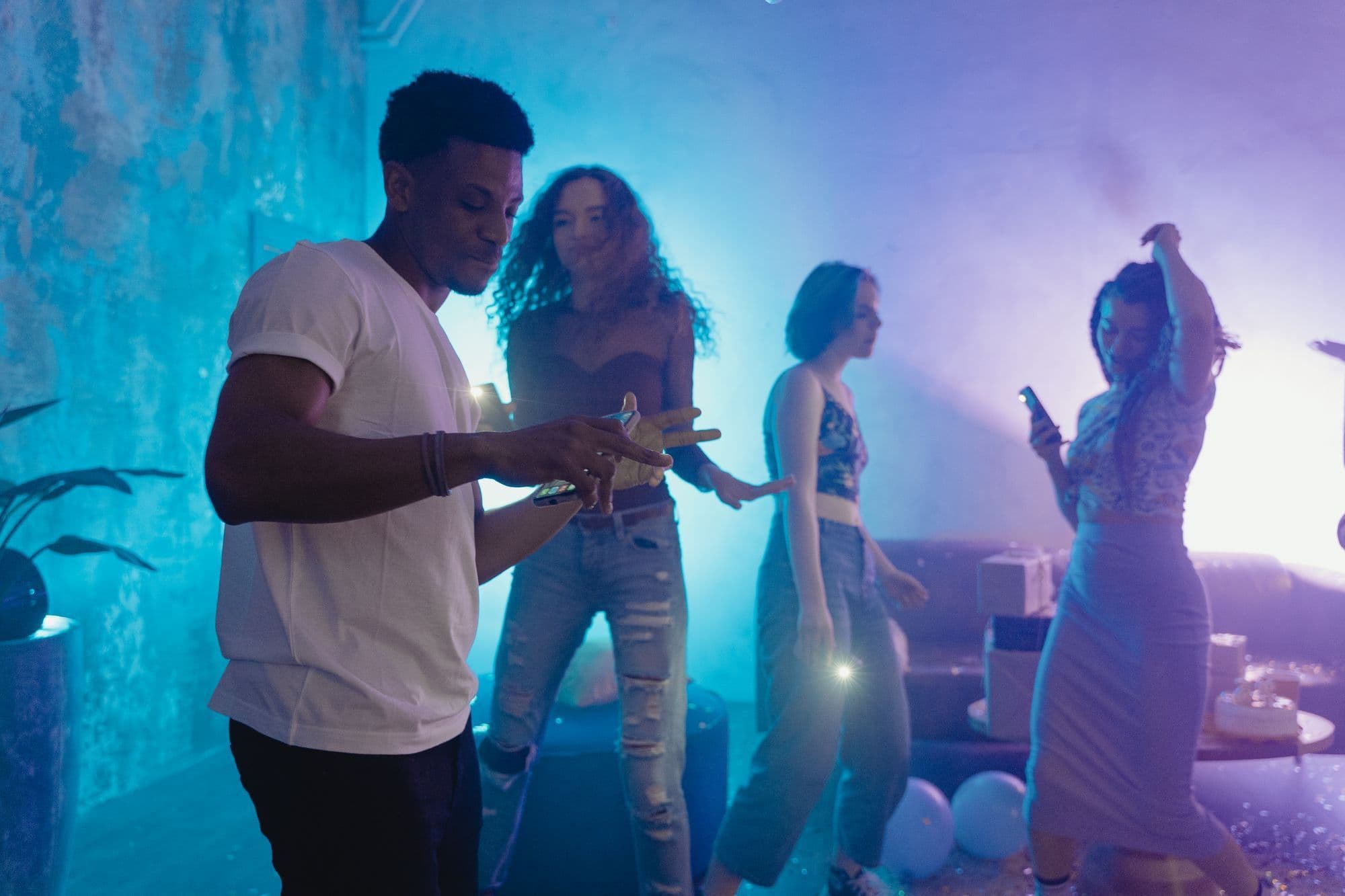 Four friends dancing in a blue-lit room with balloons on the floor