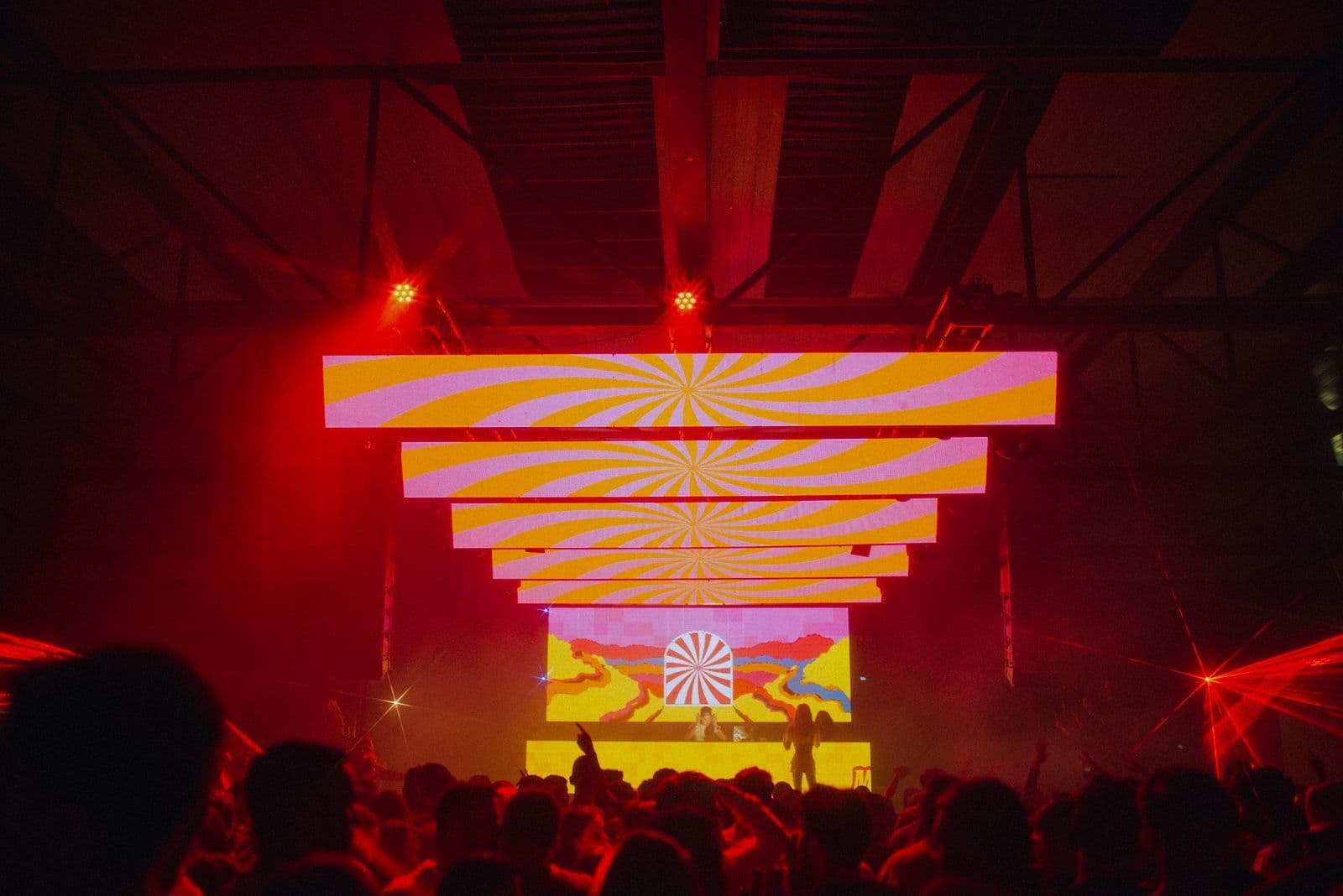 A crowd facing a glowing LED stage inside a dark warehouse party