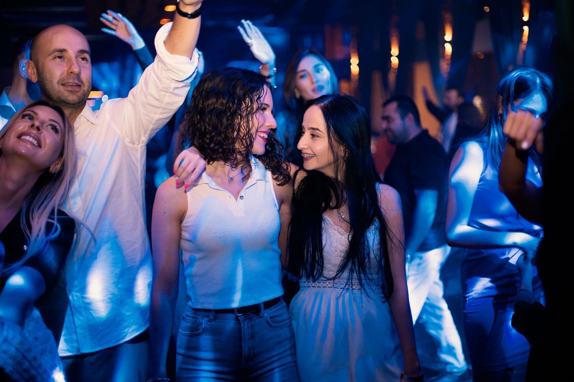 Friends dancing close together with arms around each other on a club floor under blue light