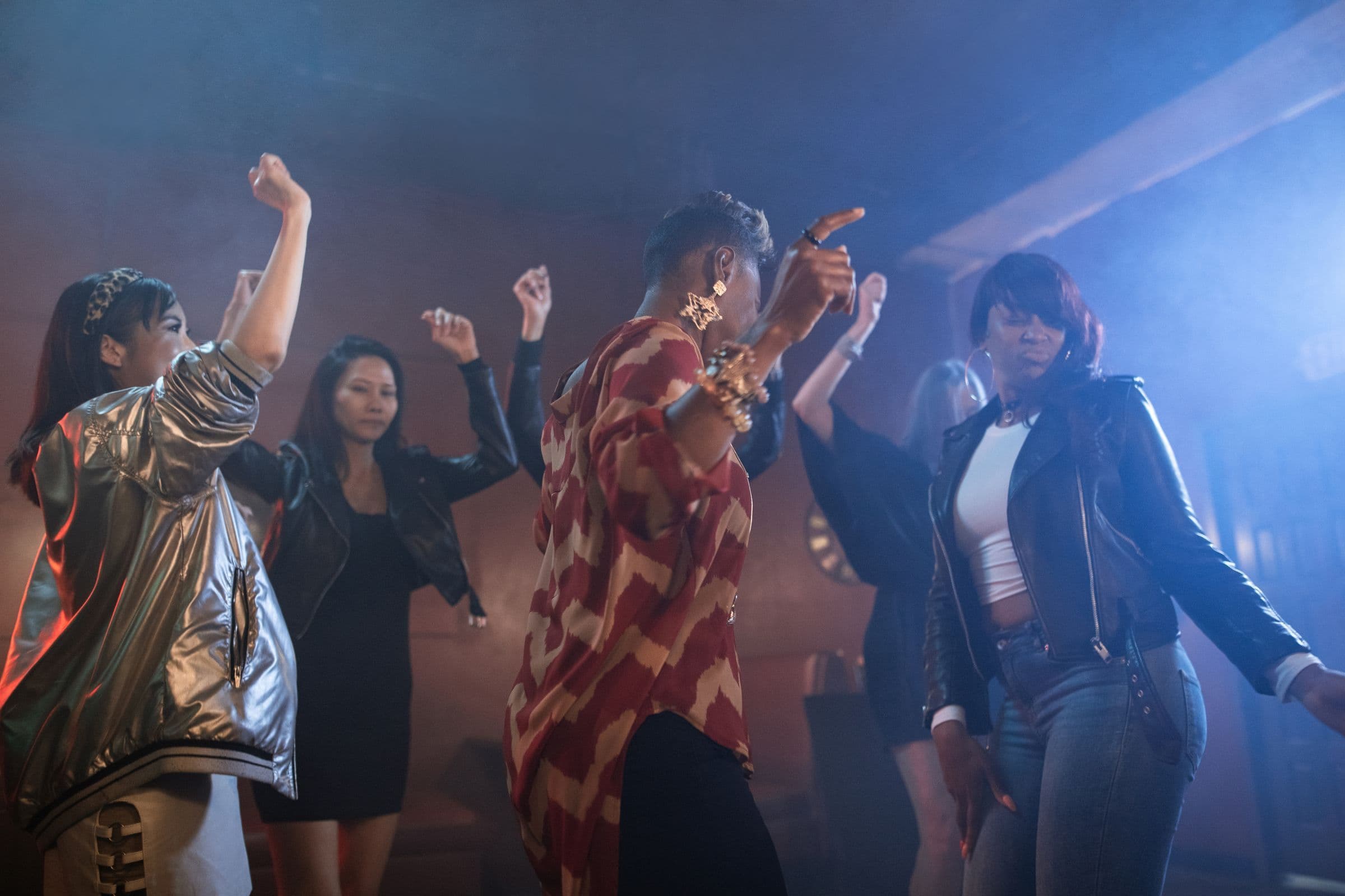 A diverse group of friends dancing with their hands up on a hazy, blue-lit club dance floor