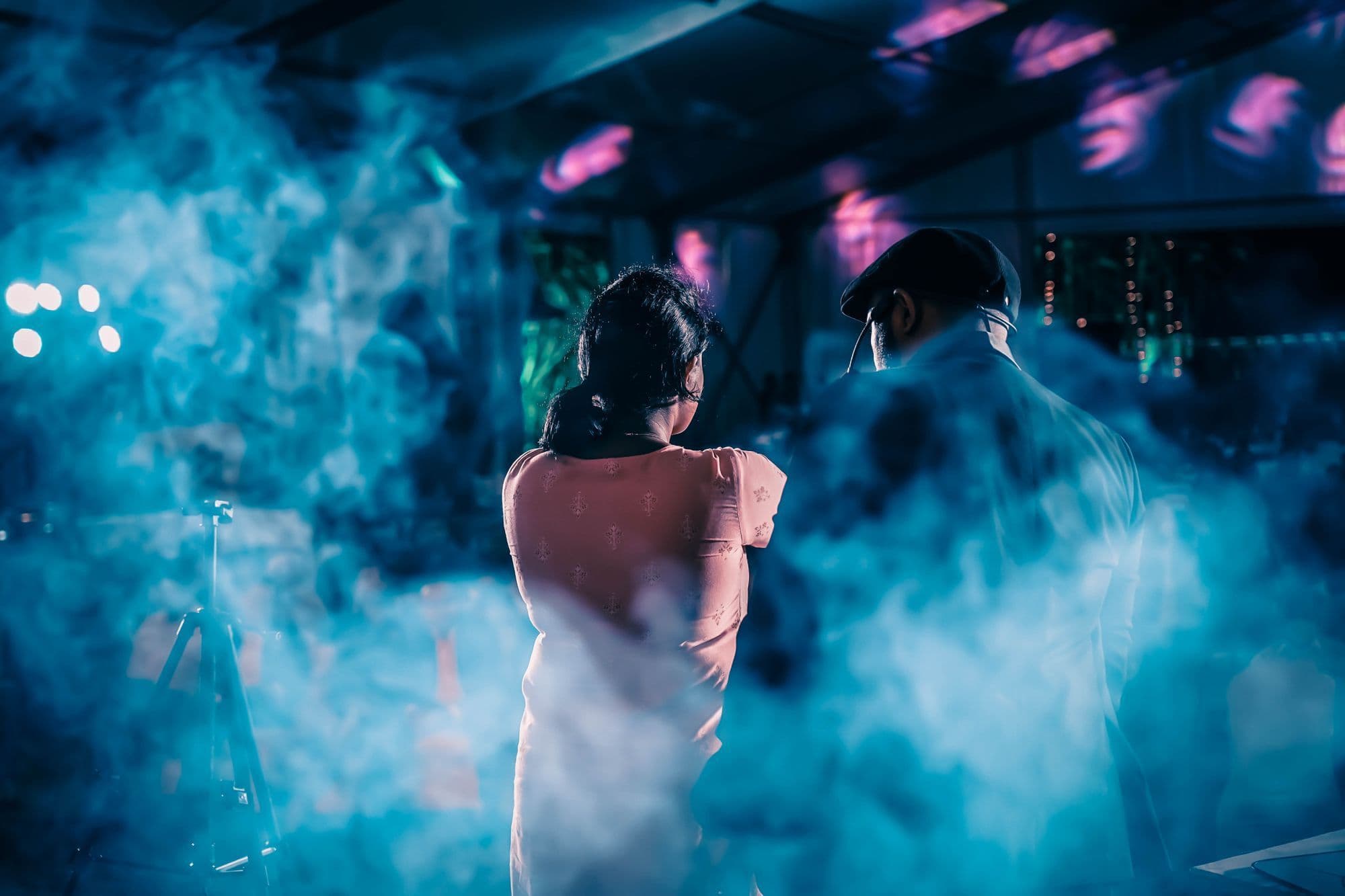 A woman and a man seen from behind, standing in blue haze under stage lights