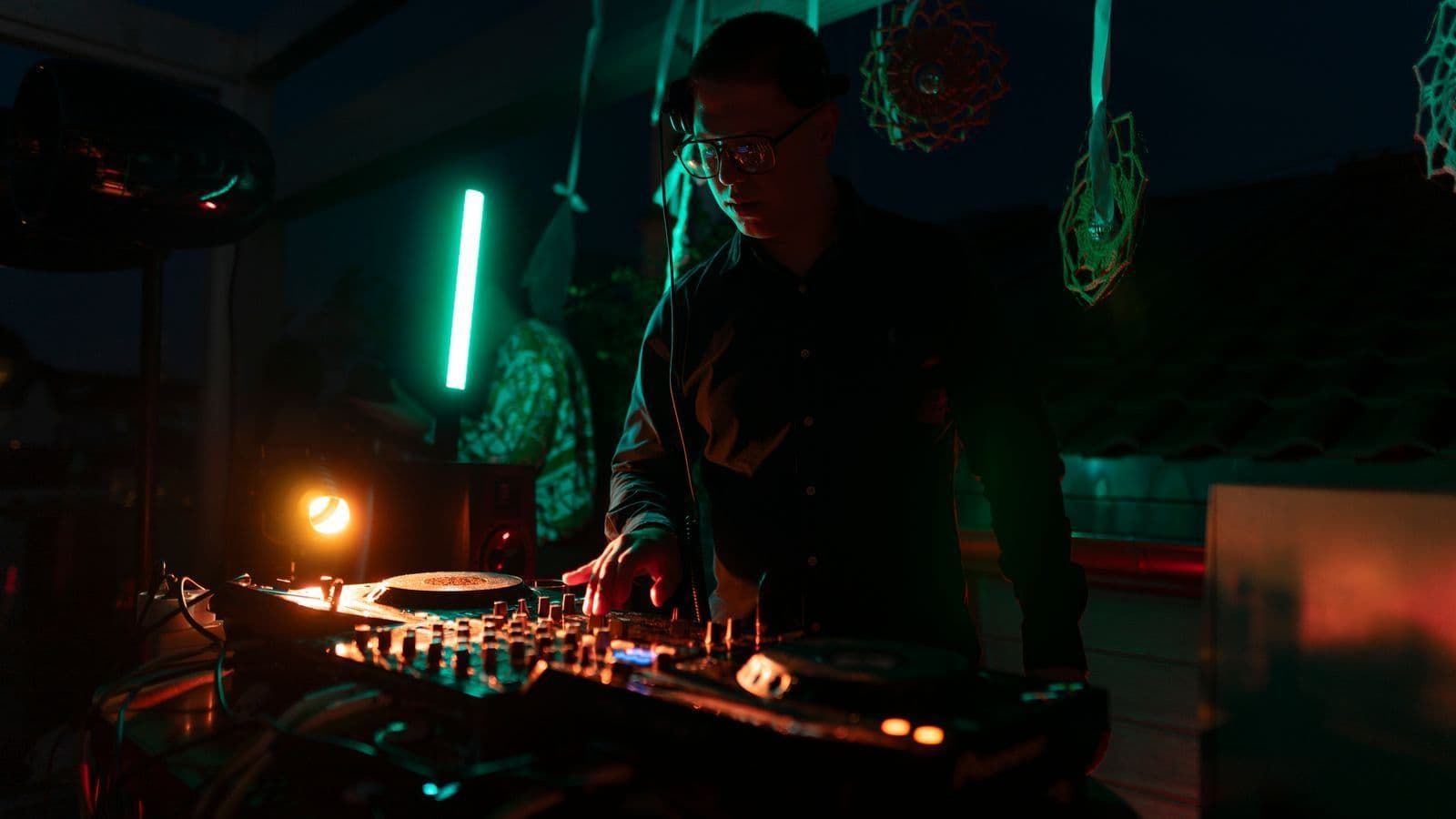 DJ mixing at a dimly lit booth with green light behind him