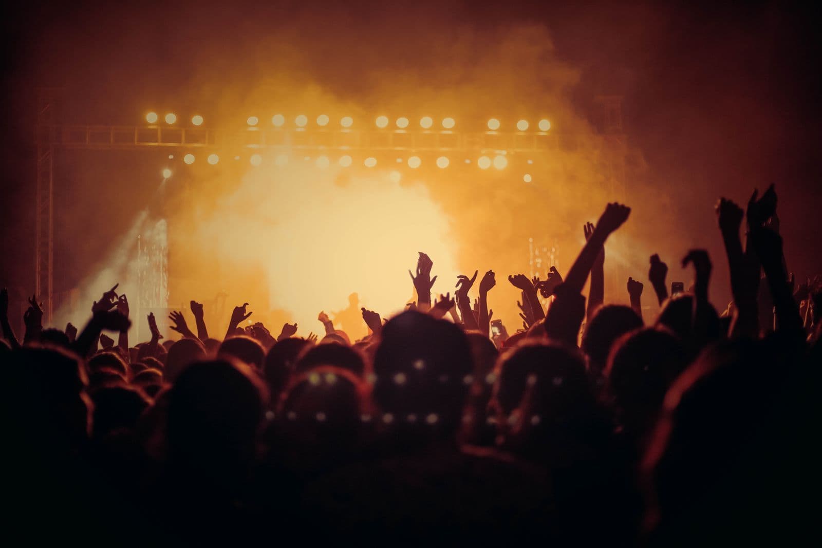 Crowd facing a bright stage under warm orange lights with hands raised