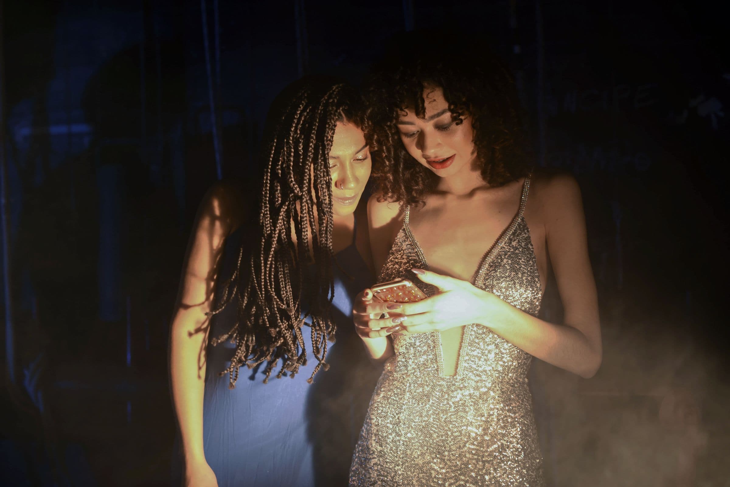 Two friends checking a phone together in a dark, smoky venue