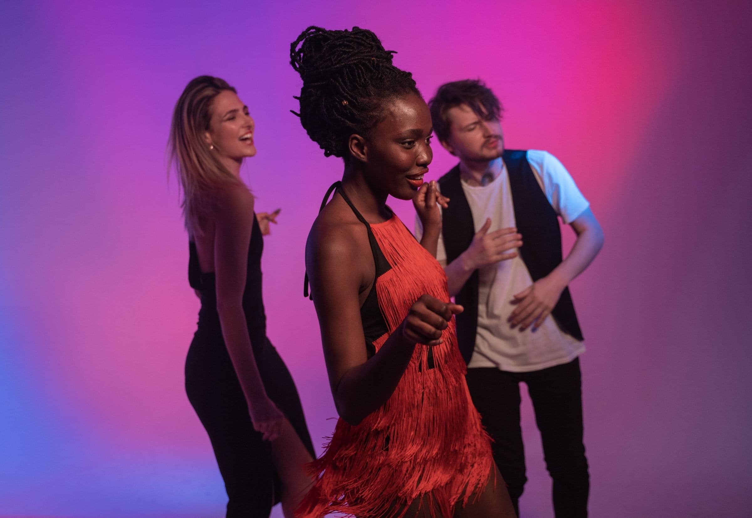 Three friends dancing together under pink and purple party lights