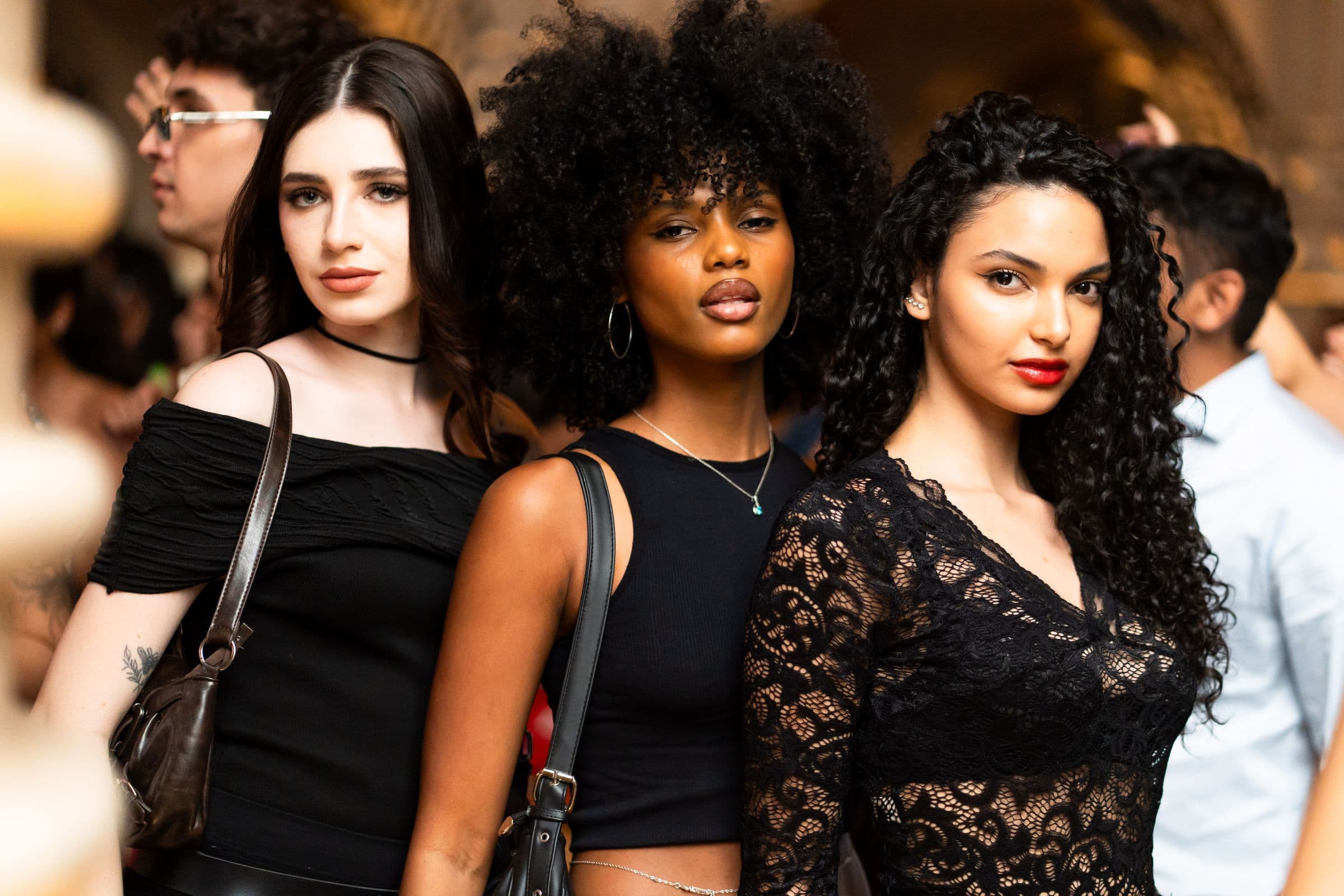 Three friends dressed in black standing close together at a crowded evening event