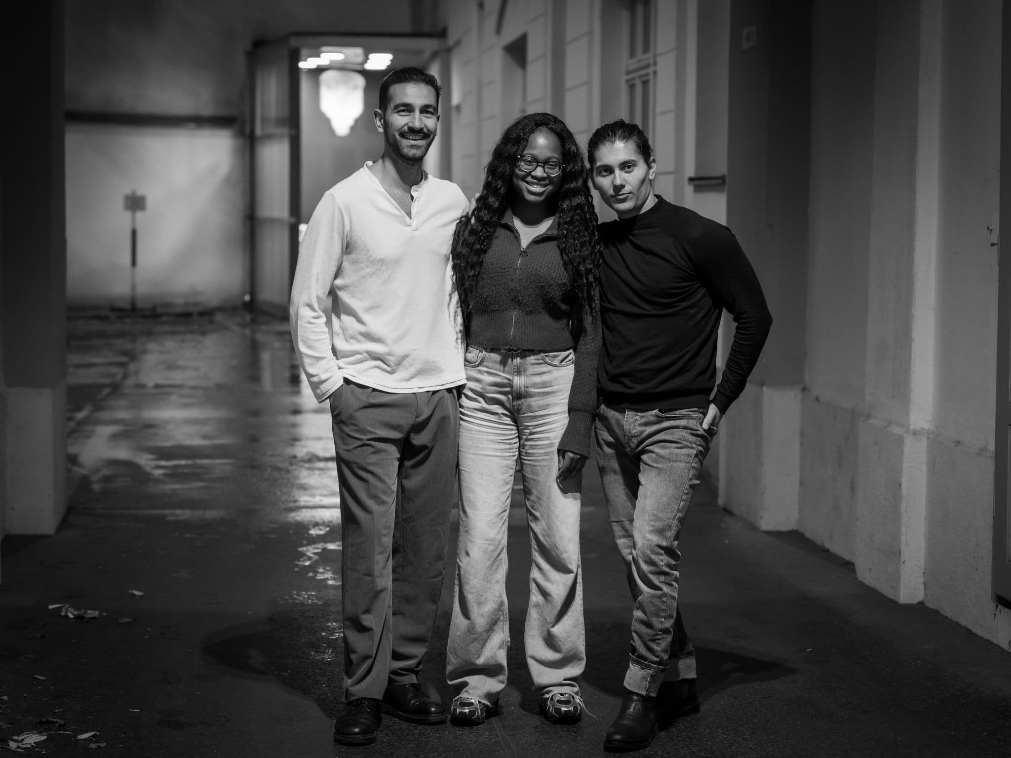 Black-and-white photo of three friends standing close together in a city passage at night