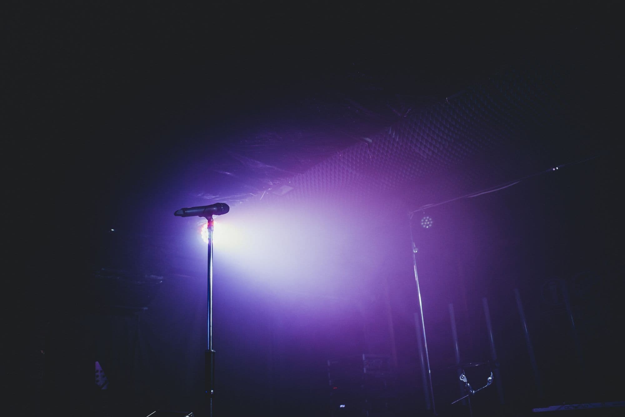 Microphone on a stand lit by a purple stage light on an empty stage