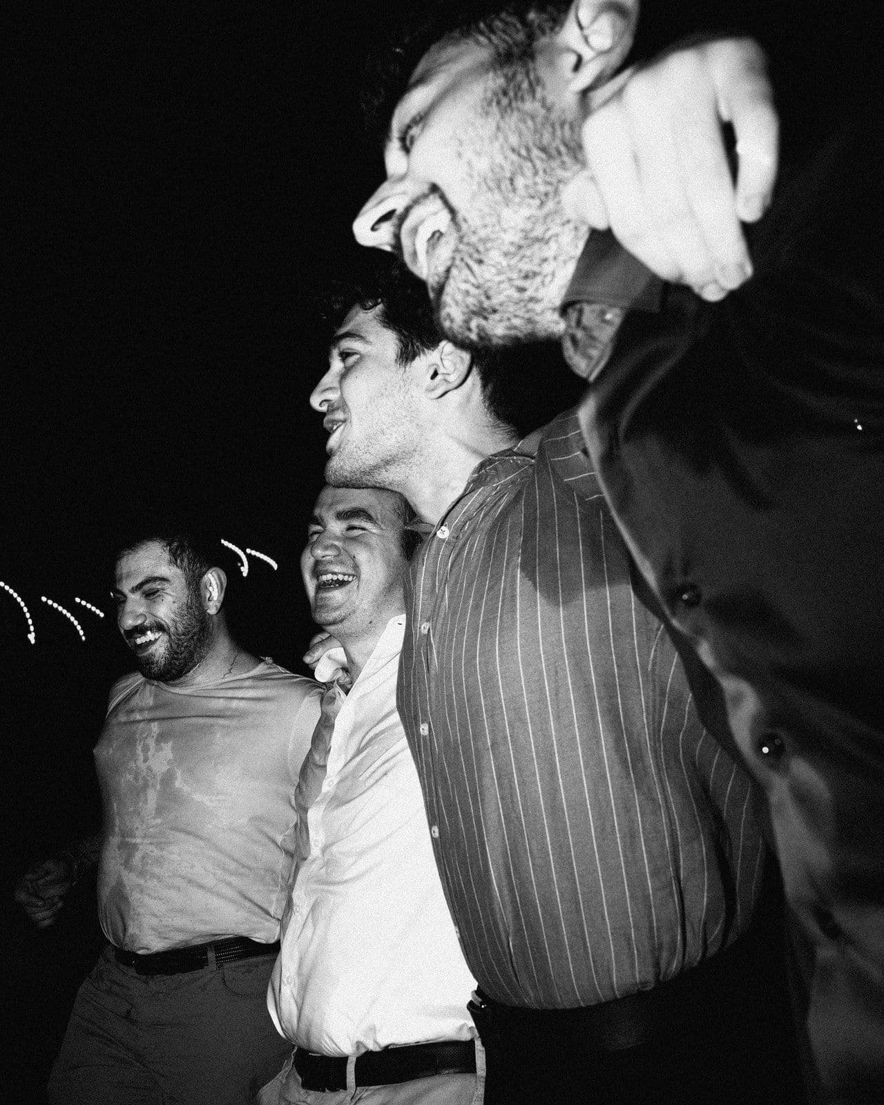 Four friends laughing with their arms around each other at a party at night, in black and white
