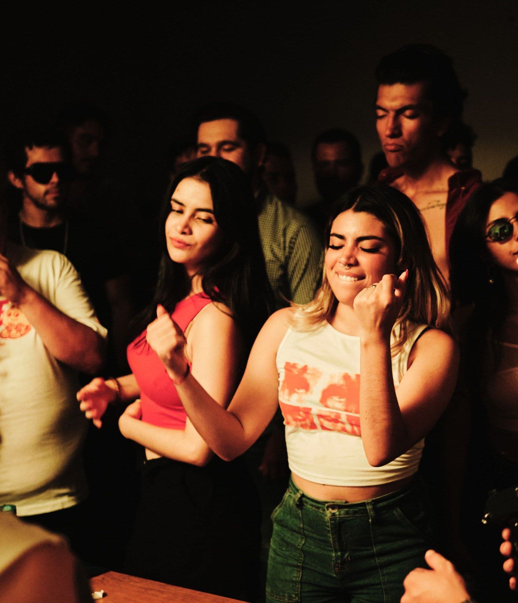 A crowd dancing with their eyes closed in a dark, warmly lit room