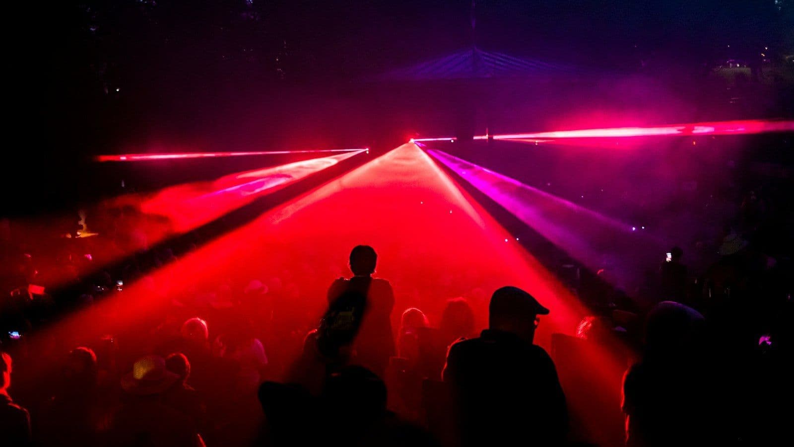 Crowd dancing under red and pink laser beams on a packed club night
