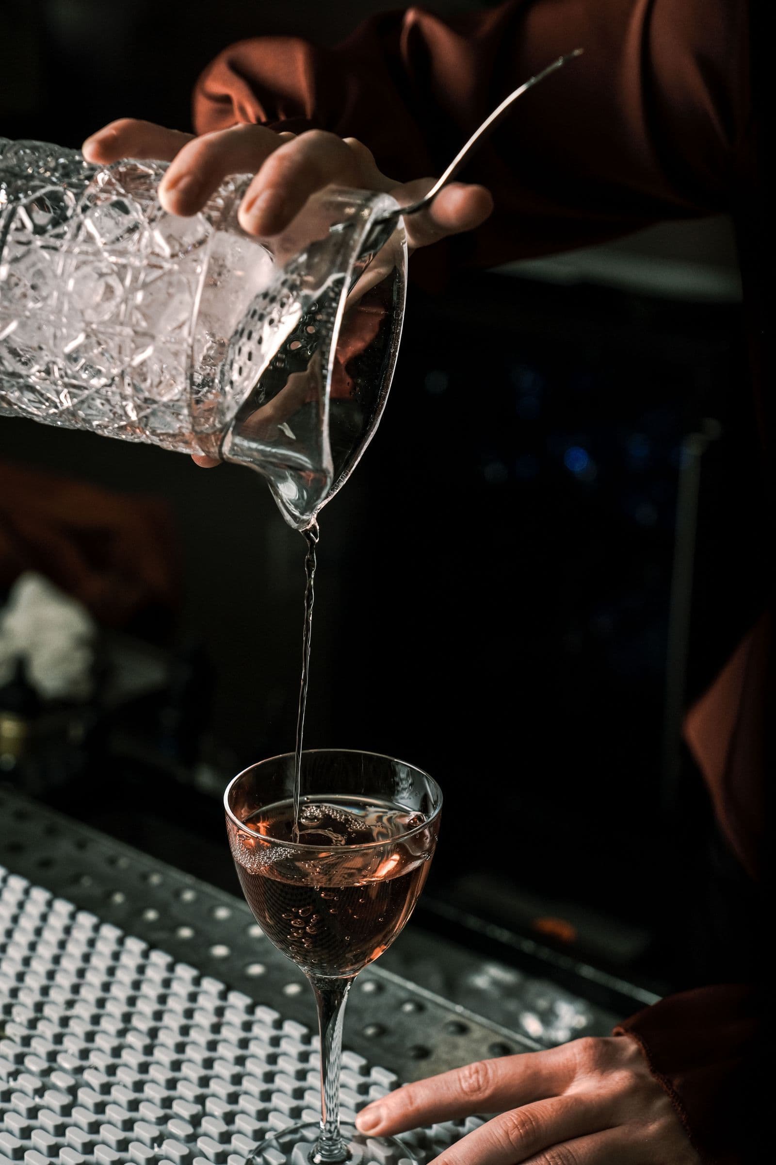 Bartender pouring a cocktail from a mixing glass in a dimly lit bar