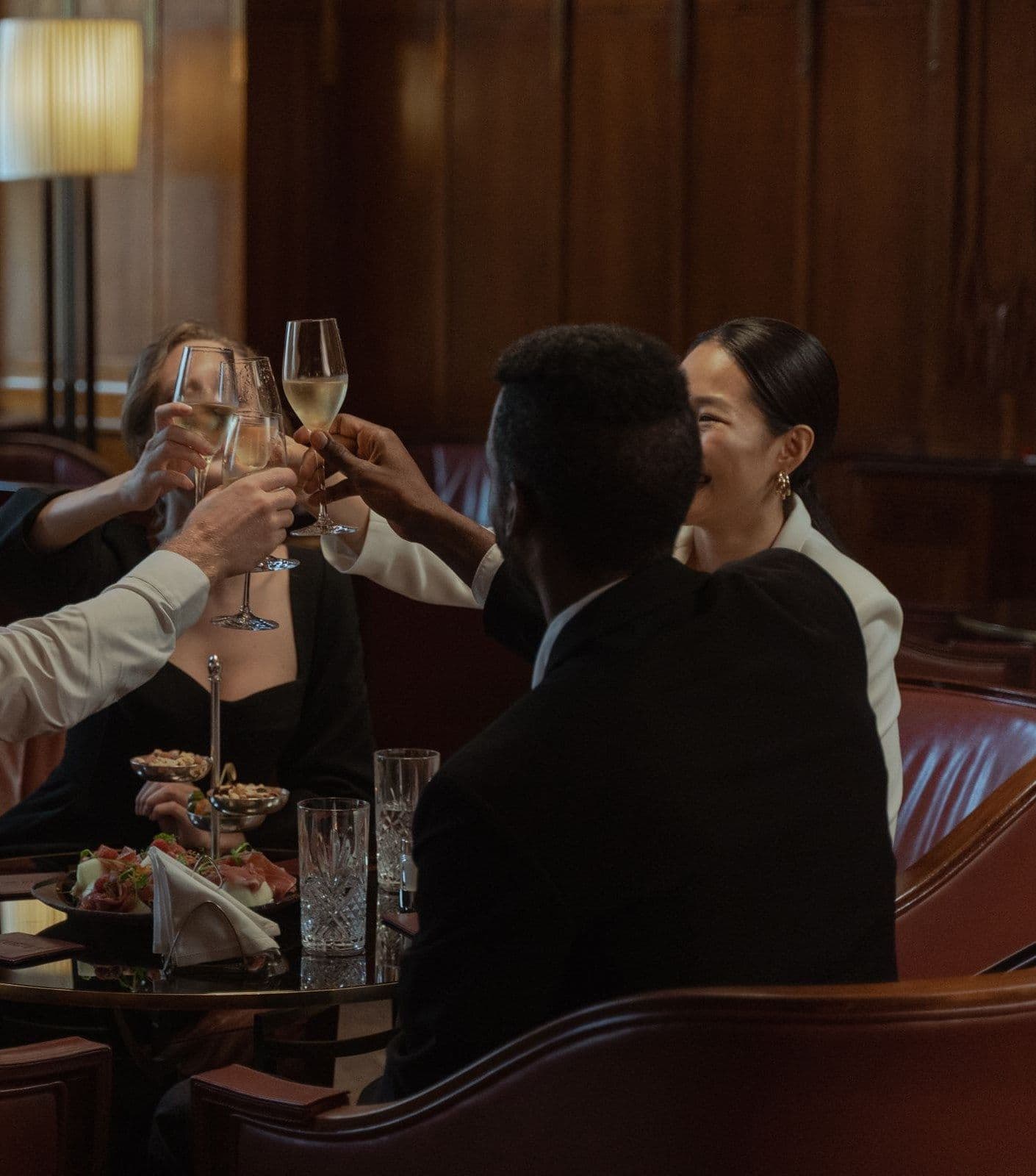 Friends of different backgrounds raise their glasses for a toast at a dimly lit lounge table