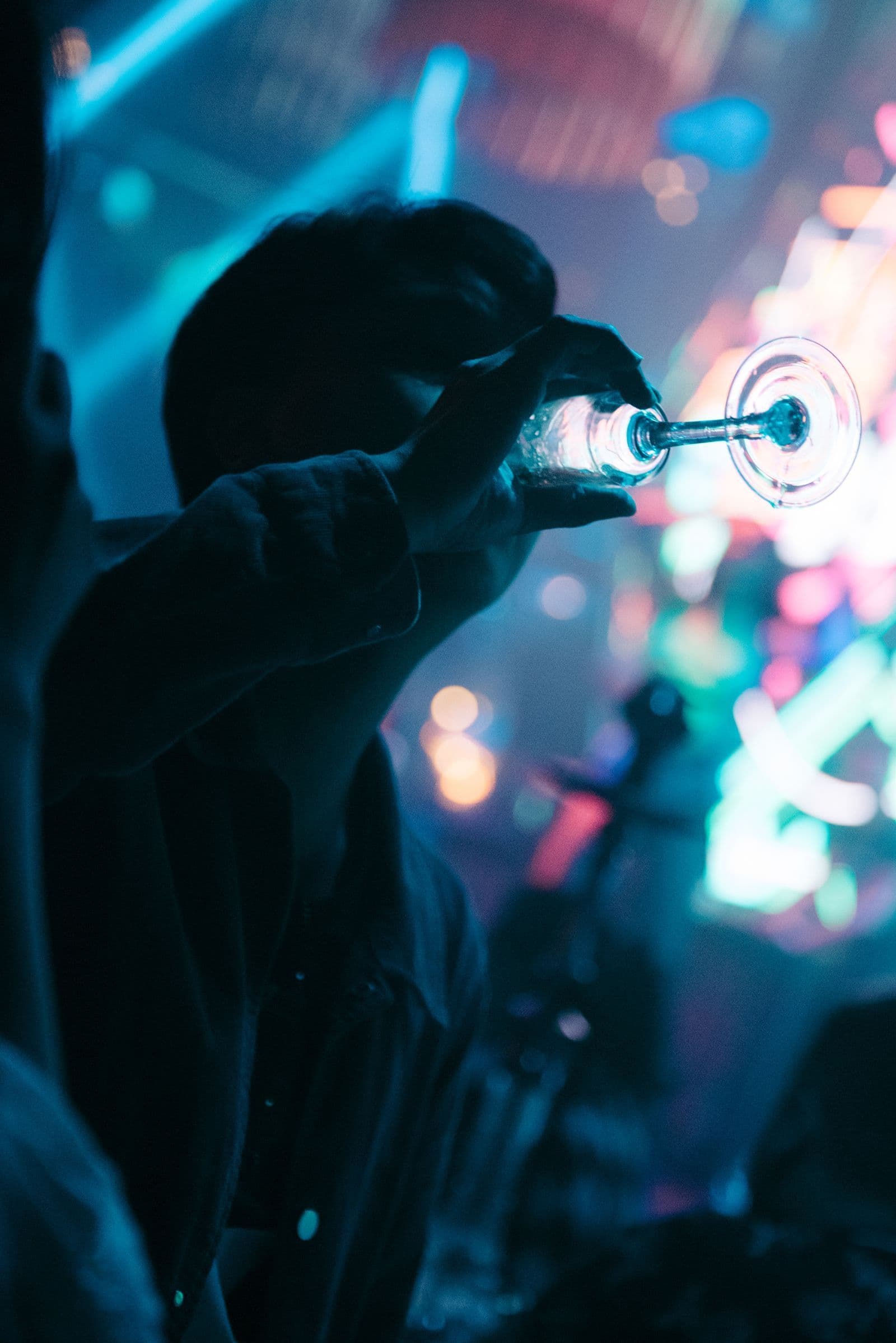 Silhouette of a guest drinking from a coupe glass under blue and pink club lights